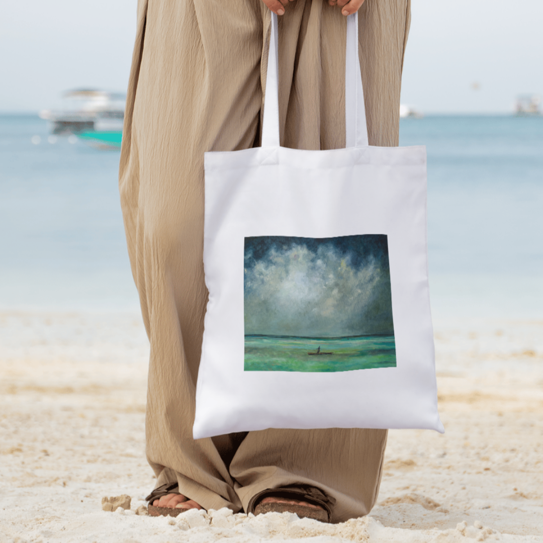 Person holding a tote bag with a beach scene design on a sandy background