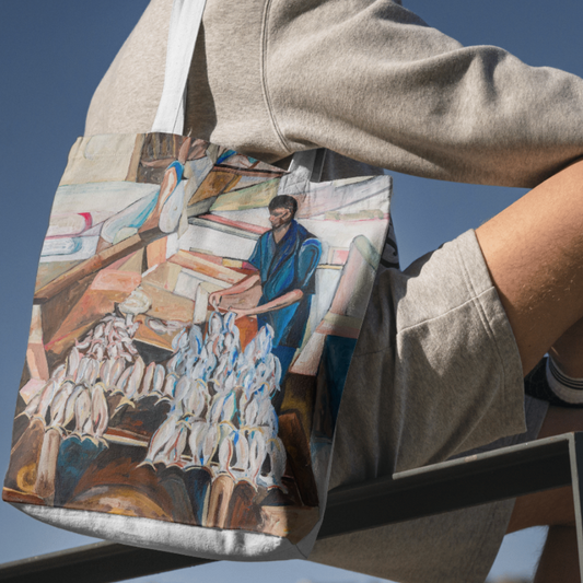 Person wearing a beige hoodie and shorts, holding a tote bag with a painting of a man working with fish.